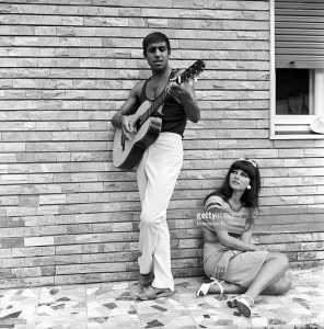 Italian singer and actor Adriano Celentano playing the guitar near his wife, Italian actress Claudia Mori (Claudia Moroni). Le Focette, August 1967