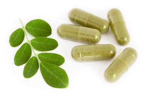 Moringa oleifera capsule with green fresh leaves on white background