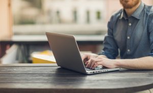 Unrecognizable man using a modern portable computer on an outdoor table, street on background